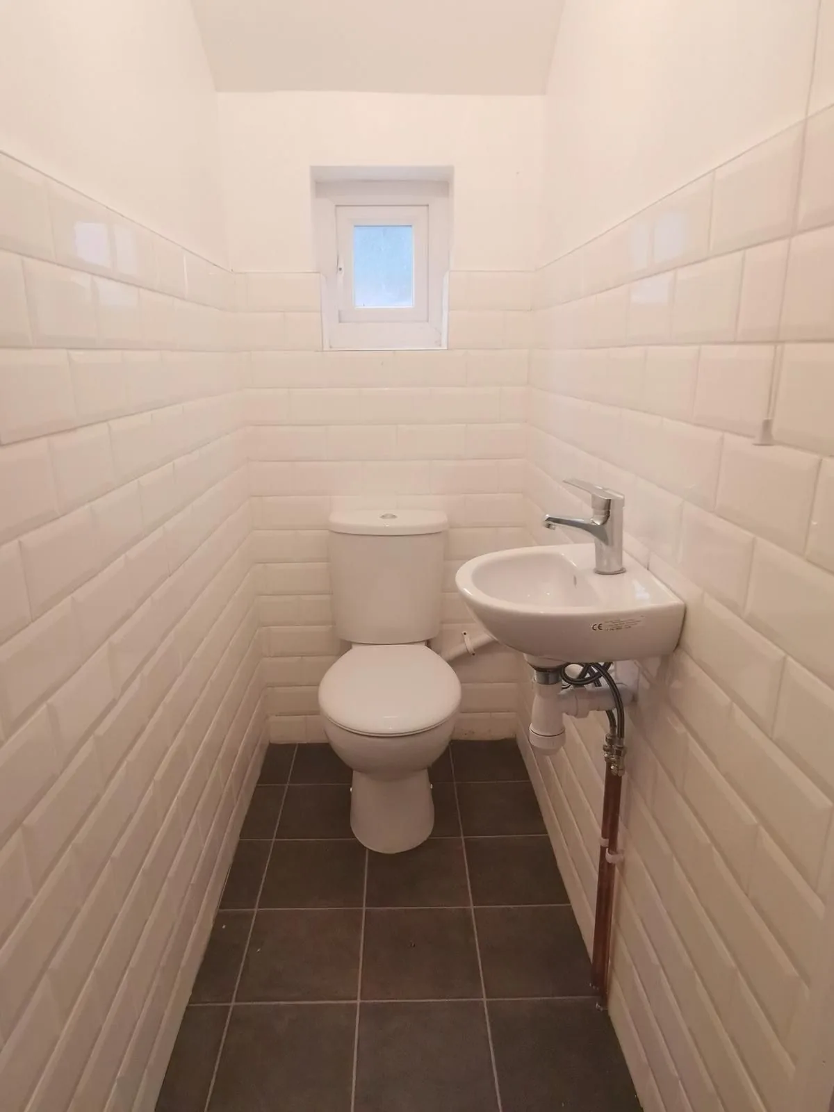 A new first floor WC tiled in white metro tiles, with a close coupled toilet and a wall hung basin on new pipework