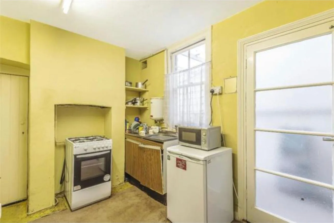 A dated kitchen before refurbishment, with a freestanding gas cooker standing in the old chimney recess