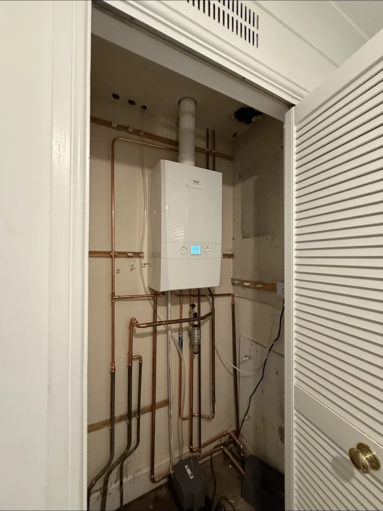 A combi boiler installed inside a ventilated hallway cupboard with new copper pipework below.