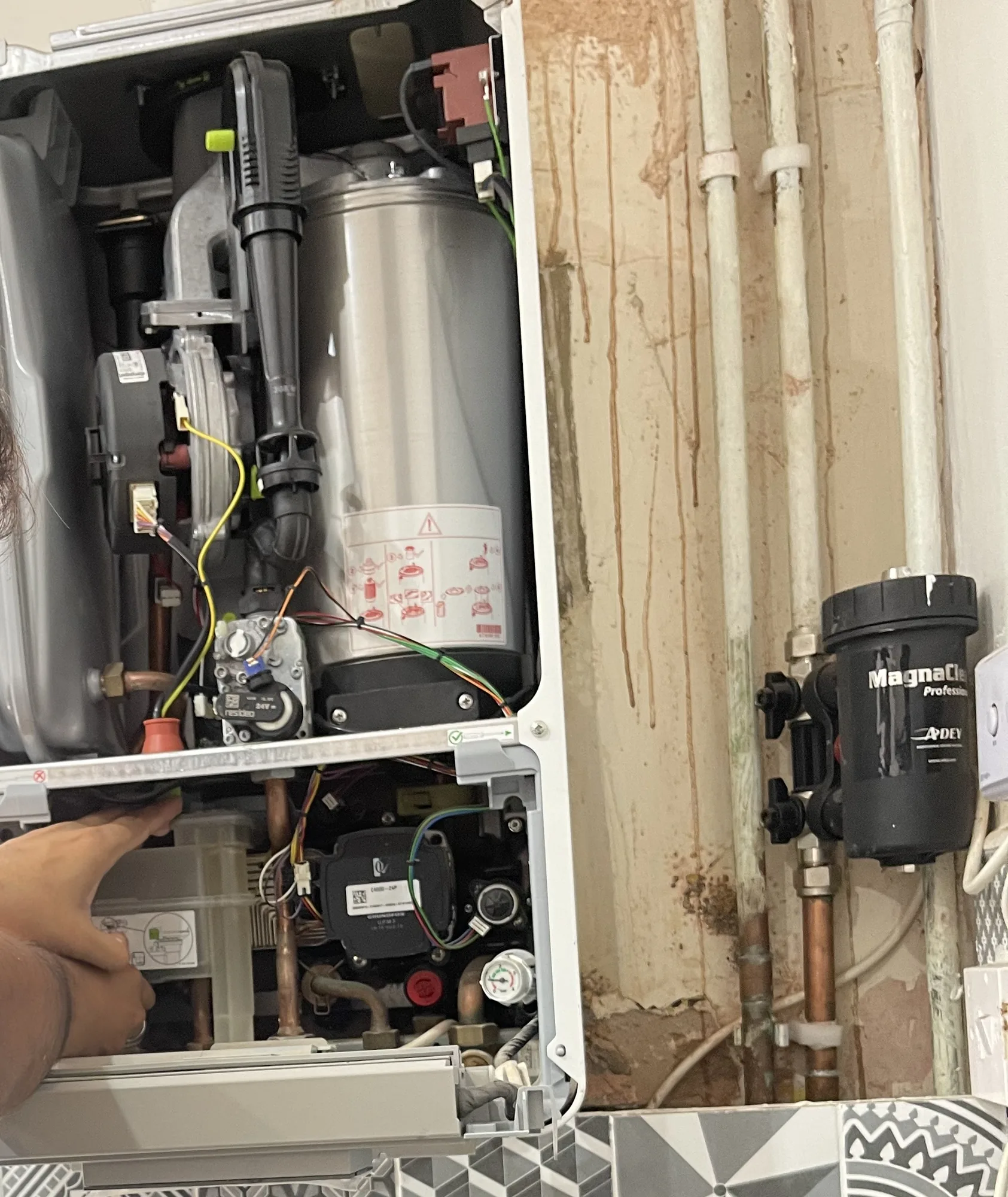 The inside of an open boiler during a central heating repair, with the gas valve, fan and magnetic system filter visible.