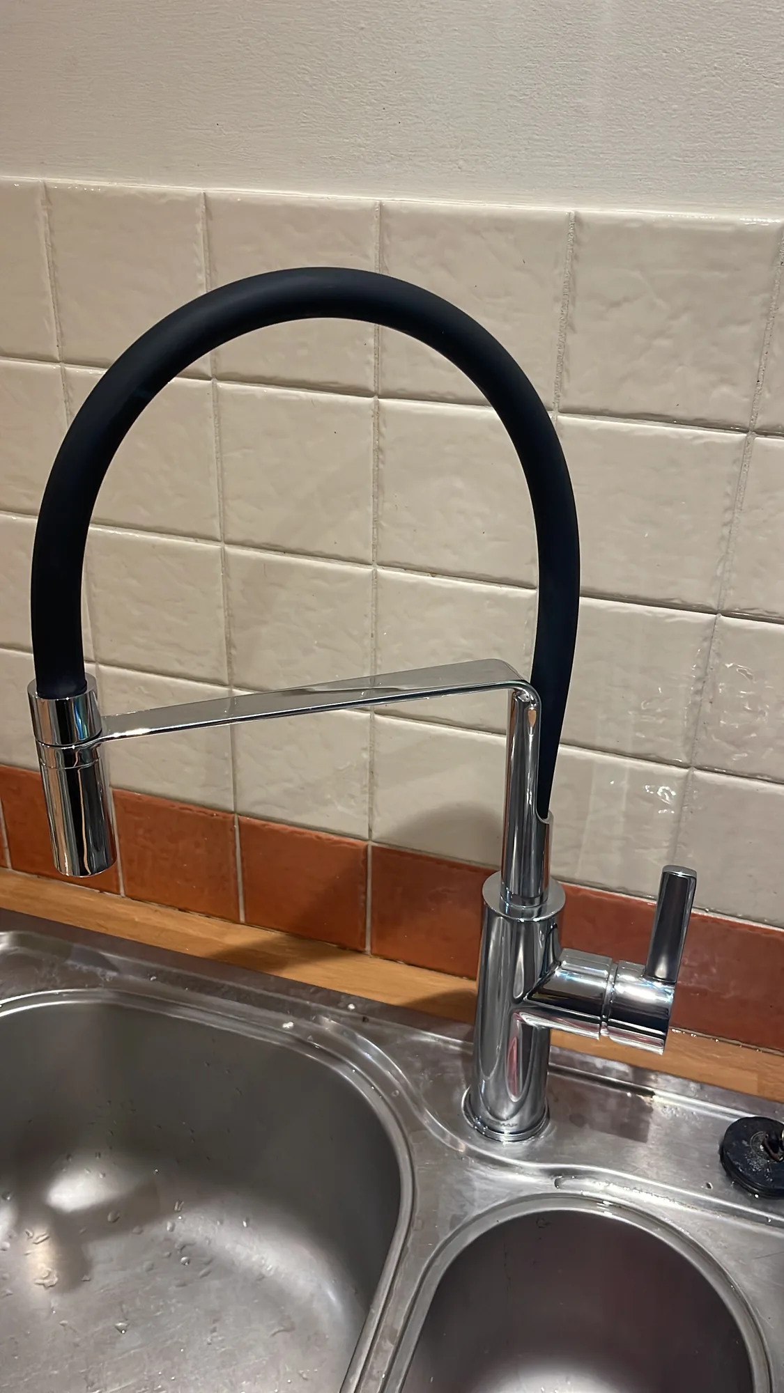 A newly fitted chrome kitchen mixer tap with a flexible spout on a stainless steel double bowl sink.