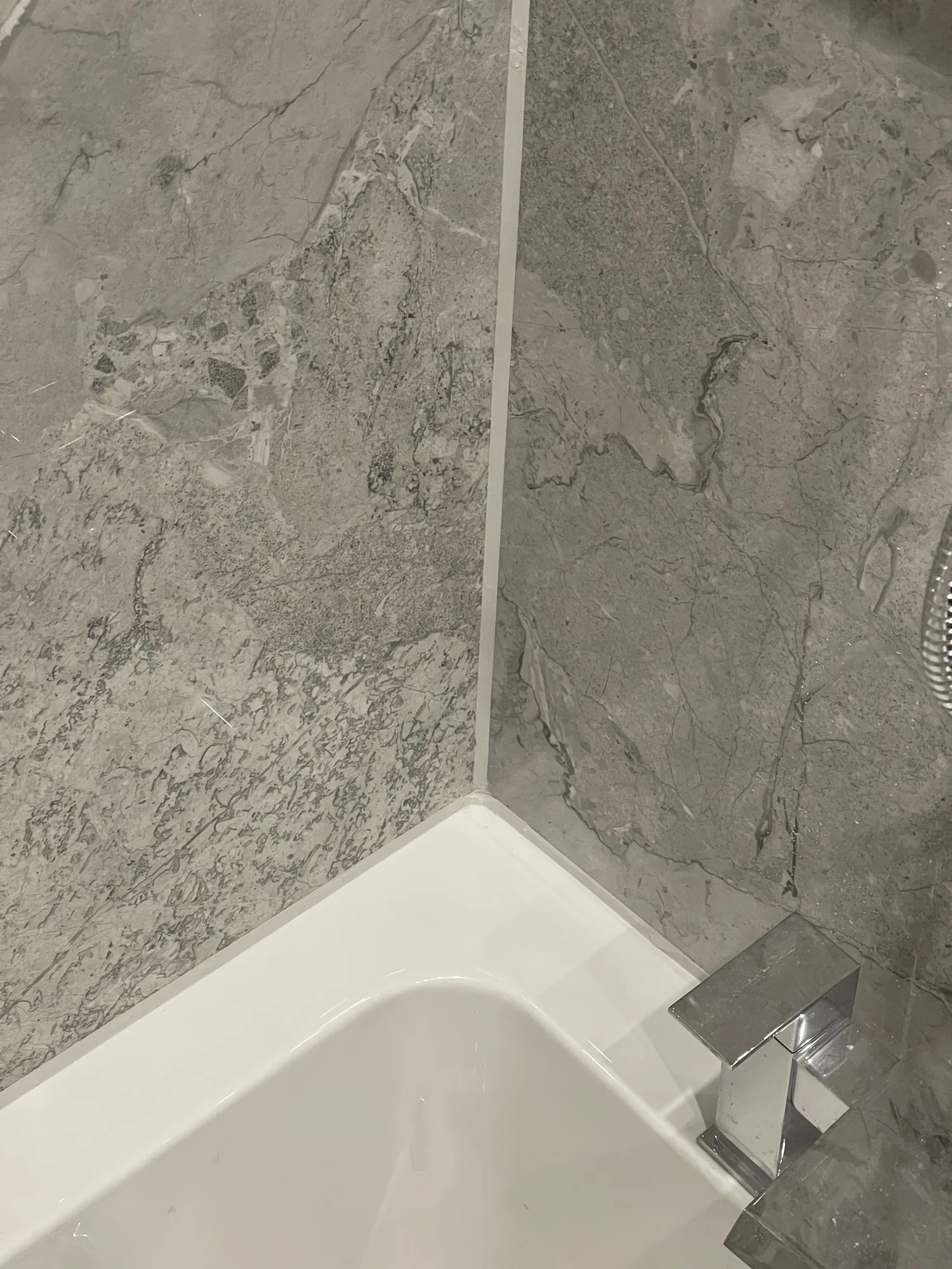 A square chrome bath filler against grey marble effect tiling in a newly fitted bathroom.