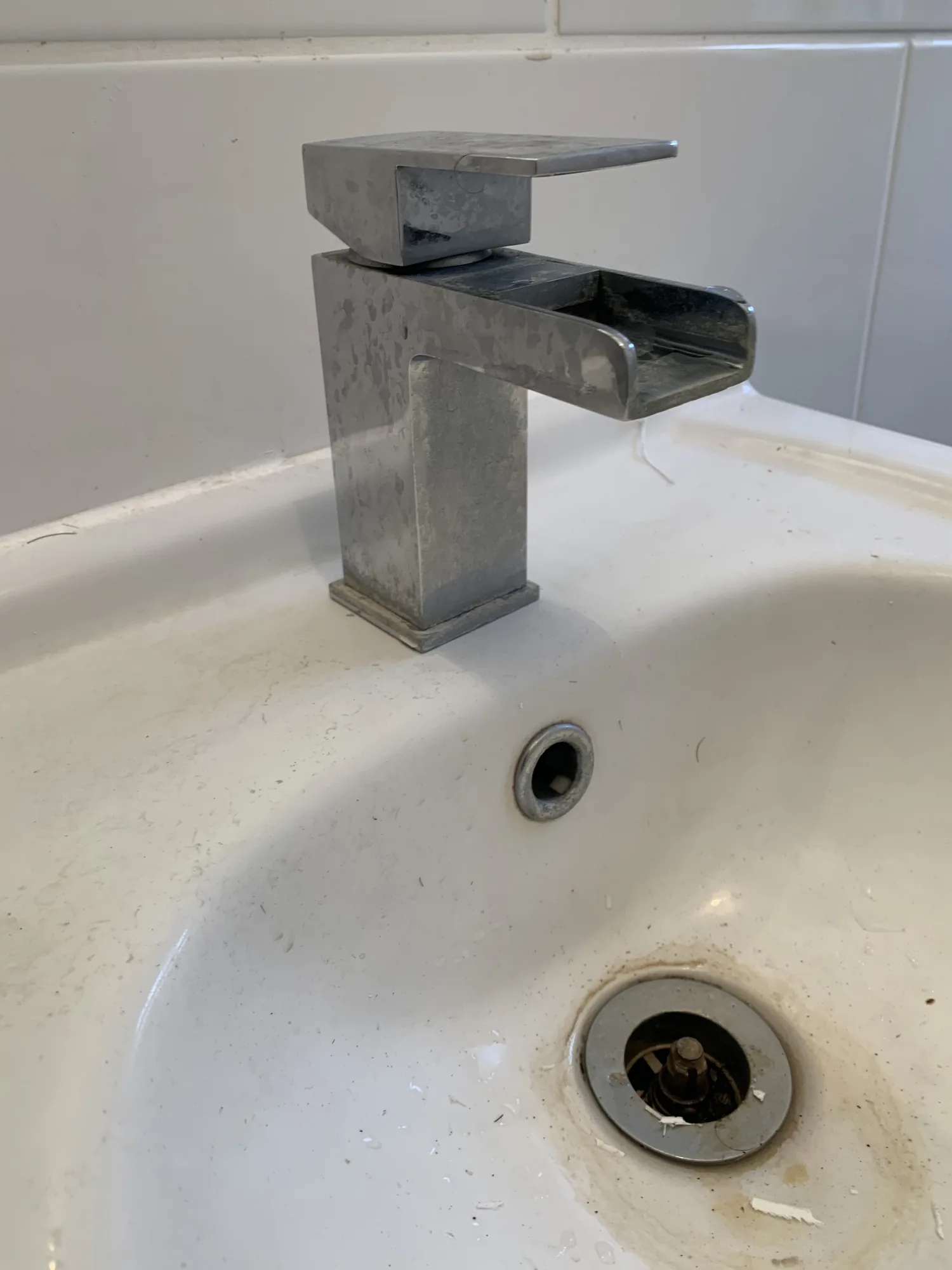 A square chrome waterfall basin mixer tap checked over during a bathroom plumbing repair.